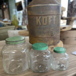 Oude glazen voorraadpotten met groene deksels in drie verschillende maten, ideaal voor het opbergen van etenswaren.