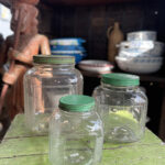 Oude glazen voorraadpotten met groene deksels in drie verschillende maten, ideaal voor het opbergen van etenswaren.