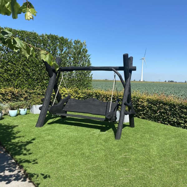 Een prachtige zwarte houten schommel die aan de rand van een weiland staat
