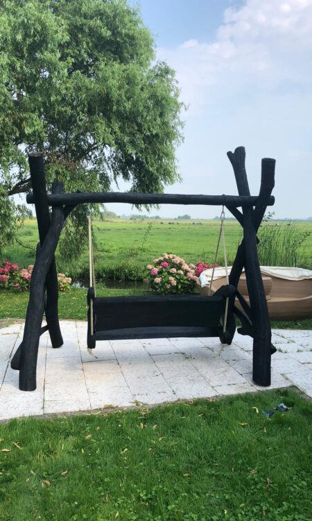 Deze zwarte houten schommelbank is gemaakt van eiken zitgedeelte en acacia palen. Doordat de vormen van de planken organisch zijn heeft elke schommel zijn unieke karakter. De schommel is in een zwarte beschermende olie gezet.