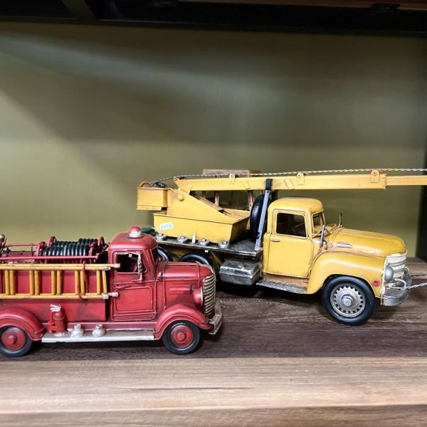Vintage blik modelauto’s van een brandweerauto en takelwagen op een houten plank als decoratie.