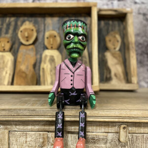 Handgemaakte houten bungelpop in Frankenstein stijl met beweegbare benen zittend op een kast.