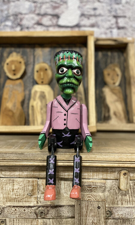 Handgemaakte houten bungelpop in Frankenstein stijl met beweegbare benen zittend op een kast.