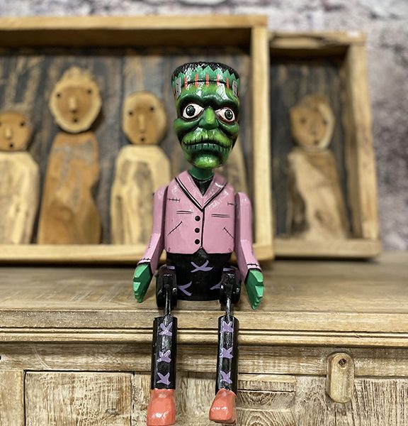 Handgemaakte houten bungelpop in Frankenstein stijl met beweegbare benen zittend op een kast.