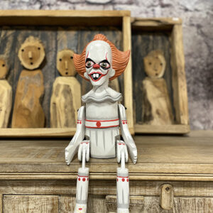 Handgemaakte houten bungelpop van een horror clown met beweegbare benen zittend op een kast.