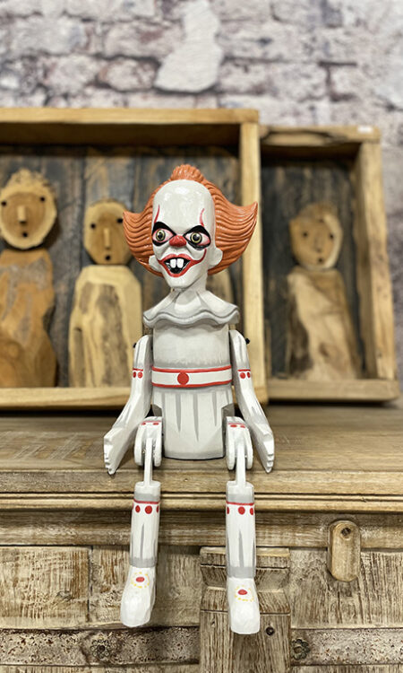 Handgemaakte houten bungelpop van een horror clown met beweegbare benen zittend op een kast.