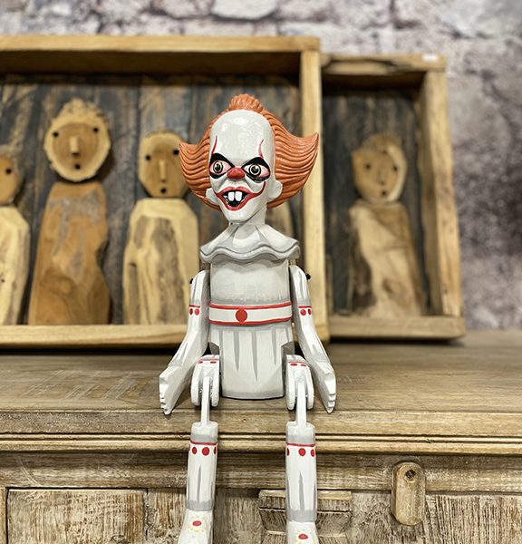 Handgemaakte houten bungelpop van een horror clown met beweegbare benen zittend op een kast.